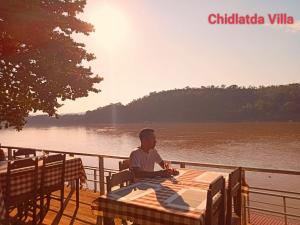 Un uomo seduto a un tavolo vicino all'acqua di Mekong Chidlatda Villa a Luang Prabang