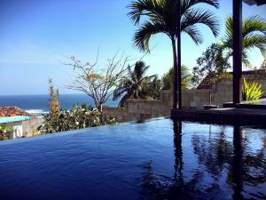 a swimming pool with palm trees and the ocean at Villa Alcheringa Yogyakarta in Yogyakarta