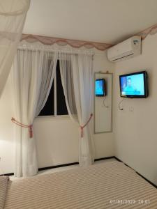a bedroom with a bed with white curtains and a tv at apartamento som do mar in Fortaleza
