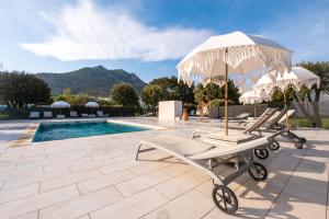 a group of chairs and an umbrella next to a pool at Hôtel & Restaurant Les Mouettes in Belgodère