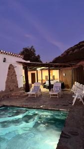 una piscina con 2 sillas y una casa en Cortijo Borreguero en Villanueva del Trabuco