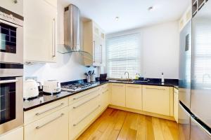 a kitchen with white cabinets and a wooden floor at Stylish 4 bedroom house with a patio and parking in London