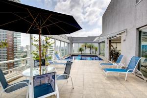 un patio con sillas, una sombrilla y una piscina en Roomo Etoile GeorgeV Itaim Bibi Residencial, en São Paulo