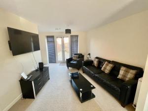 a living room with a black leather couch and a flat screen tv at Silver Stag Properties, Comfy 2 BR Home in Ashby in Smisby