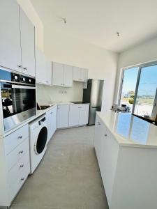 a kitchen with white cabinets and a large window at WaveBreeze Villas in Paphos City