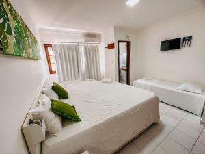 um quarto com uma grande cama branca com almofadas verdes em A 200m da praia de Taperapuã, (Axé Mói) 2 suítes piscina, sauna, portaria 24hrs internet privativa 300MBPS em Porto Seguro