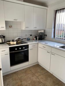 una cocina con armarios blancos y horno negro en Spencer Court en Hornchurch