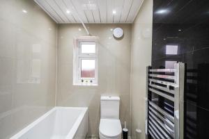 uma casa de banho com uma banheira, um WC e uma janela. em Exquisite London Home - Parking - Sleeps 10 em Dagenham