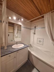 ein Badezimmer mit einem Waschbecken, einer Badewanne und einem Spiegel in der Unterkunft Studio Les 3 Lys Auron in Auron