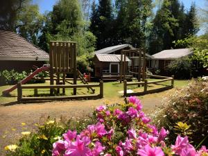 a playground with two wooden chairs and pink flowers at Cabañas Loncotraro in Pucón