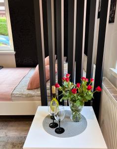 a table with two glasses and a vase with red flowers at Apartament Stary Zdroj Polanica Resort in Polanica-Zdrój