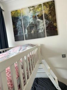 a crib in a bedroom with three paintings on the wall at Luton Airport £40 per night, best value in Luton