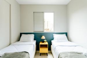 two twin beds in a room with a yellow night stand at Super bem localizado, no centro, com varanda! in Poços de Caldas