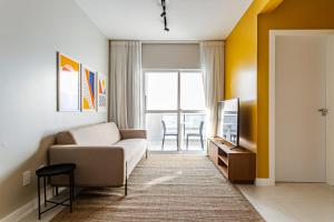 a living room with a couch and a tv at Prédio com apartamentos completos, com piscina e a passos da praia - Agua Marinha in Florianópolis