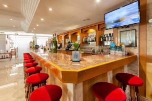 un bar con taburetes rojos y TV en Hotel Amoros, en Cala Ratjada