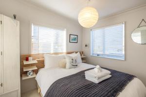 a bedroom with a bed with white sheets and windows at Welcome Cottage in Oneroa