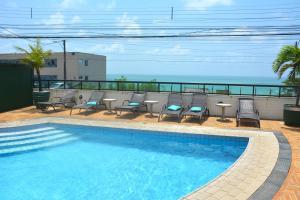 a swimming pool with chairs and a table and the ocean at Suítes Natal Plaza - Apto 1812 in Natal