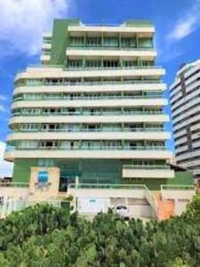 un grand bâtiment vert avec des arbres devant lui dans l'établissement 1/4 na praia de Armação, à Salvador