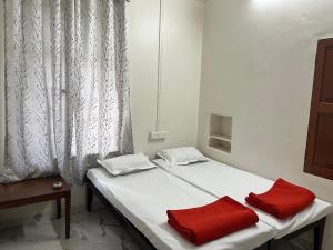 ein Bett mit zwei roten Kissen neben einem Fenster in der Unterkunft Hotel Laxminarayan Niwas in Pune