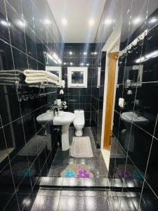 Baño de azulejos negros con aseo y lavamanos en New Park Resort, en Mahajanga