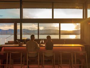 un hombre y una mujer sentados en una mesa frente a una ventana en YANMAR SUNSET MARINA CLUBHOUSE&HOTEL, en Moriyama