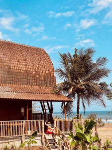 uma cabana na praia com uma palmeira em Dikaloha Surfschool and Stay em Airsatang