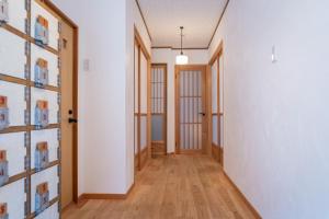 Naoshima Juju Art House　直島ジュジュアートハウス في ناووشيما: ممر به أرضيات خشبية وجدران بيضاء وأبواب خشبية