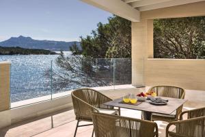 einen Tisch und Stühle auf einem Balkon mit Blick auf das Wasser in der Unterkunft 7Pines Resort Sardinia - A Destination By Hyatt in Baja Sardinia