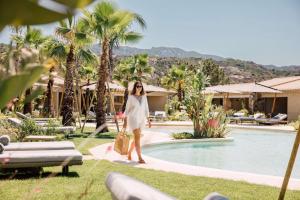 Una donna che cammina vicino alla piscina in un resort di 7Pines Resort Sardinia - A Destination By Hyatt a Baja Sardinia