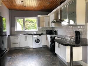 cocina con armarios blancos, lavadora y secadora en Fairway House, en Carrickfergus
