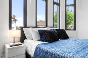 ein Schlafzimmer mit einem Bett mit einer blauen Decke und Fenstern in der Unterkunft Comfy 1BDR - 30mins to CENTRAL LDN - Parking in The Hyde
