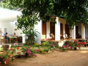 a woman sitting at a table in front of a house with flowers at Le Grand Meaulnes in Habarana