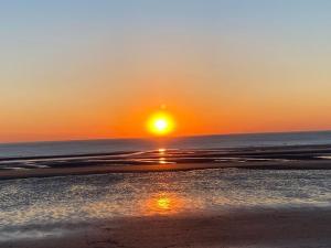 a sunset on a beach with the sun setting at Appartement cosy proche de la mer in Neufchâtel-Hardelot