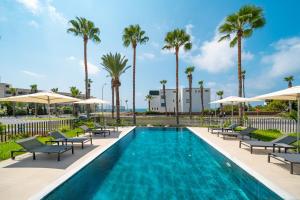 a swimming pool with chaise lounge chairs and palm trees at Waterside Sea View Apartments in Paphos City