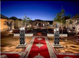 un patio con alfombra roja y 2 postes con luces en Your berber camp, en Merzouga