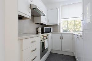 een witte keuken met witte kasten en een raam bij Cozy and bright 1 bedroom apt in Knightsbridge in Londen