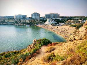 a beach with people in the water and buildings at Étoile Court Apt - homey, spacious & private patio in Mġarr