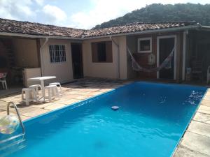 a blue swimming pool in front of a house at Casinha Sossego na Praia in Caraguatatuba