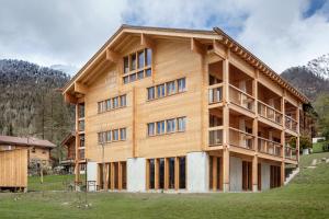 a large wooden building in a field with mountains at Berglodge Goms (Hotel) in Münster