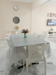 una mesa de comedor con sillas blancas y un jarrón de flores en Rafflesia Two Bedroom Pool View en Kampong Tanah Merah