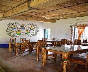 un comedor con mesas y sillas y una pintura en la pared en Khoai Village Resort en Shānti Niketan