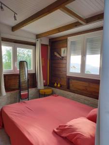 - une chambre avec un lit rouge dans une pièce dotée de fenêtres dans l'établissement Douceur des Hauteurs bas de villa, piscine privée, à Sainte-Luce