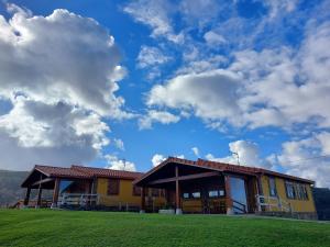a yellow house with a green field and a cloudy sky at Apartamentos El Prau in Ubiarco