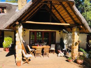 a house with a thatched roof with a table and chairs at Collie Cottage in Clarens