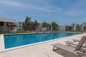 a swimming pool with two lounge chairs and buildings at Apartamento con piscina, gimnasio y acceso a playa in Punta Cana