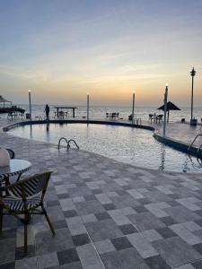 una piscina accanto alla spiaggia con una persona a piedi di فندق حدائق فرسان الفندقية a Ḩumr
