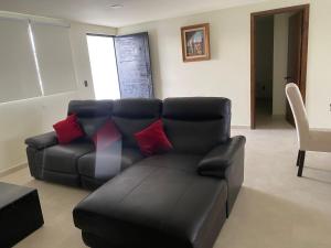 a living room with a black leather couch and red pillows at Bonito y Cómodo Departamento in Zacatecas