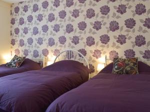 two beds in a bedroom with purple sheets and flowers on the wall at Robins Nest in Samlesbury