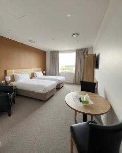 Cette chambre d'hôtel comprend deux lits, une table et des chaises. dans l'établissement Manha Hotel Auckland Airport, à Auckland