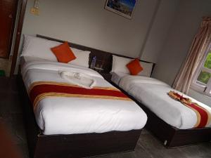 2 Betten in einem Hotelzimmer mit weißer Bettwäsche und orangefarbenen Kissen in der Unterkunft Hotel Blue moon Pokhara in Pokhara